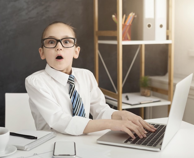 Too much information. Shocked little girl working on laptop in office, copy space