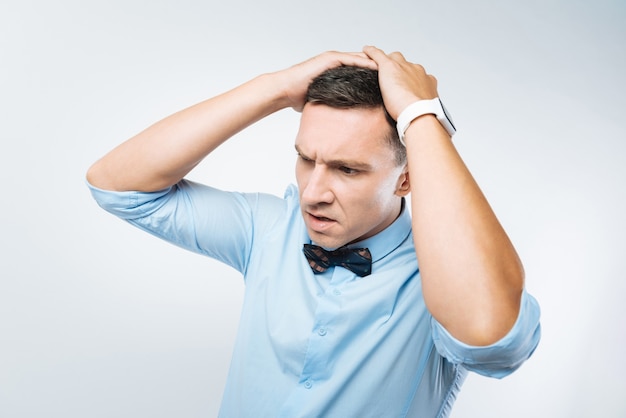 Too much stress. Unhappy depressed young man holding his head and feeling stressed out while having tough times in life