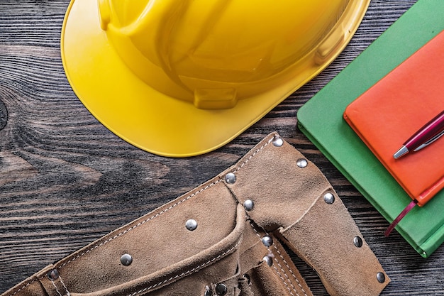 Tool belt notebooks pen building helmet on wooden board construction concept