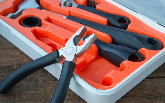 Tool kit pliers hammer screwdriver in orange plastic case on old wooden Board with copyspace