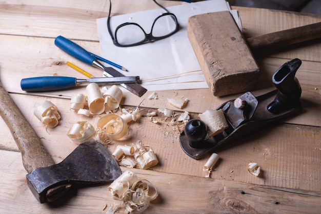 Tools carpenter on table with sawdust, planer, mallet, ax, chisel, goggles.