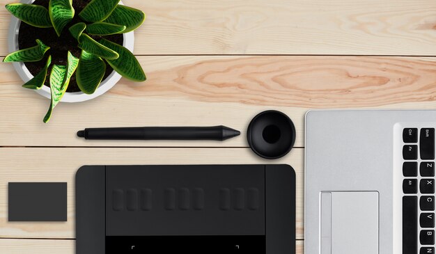 Tools of creativity. Top view of modern laptop, graphic tablet with stylus and pot with flower lying on wooden table. Photo editor work space