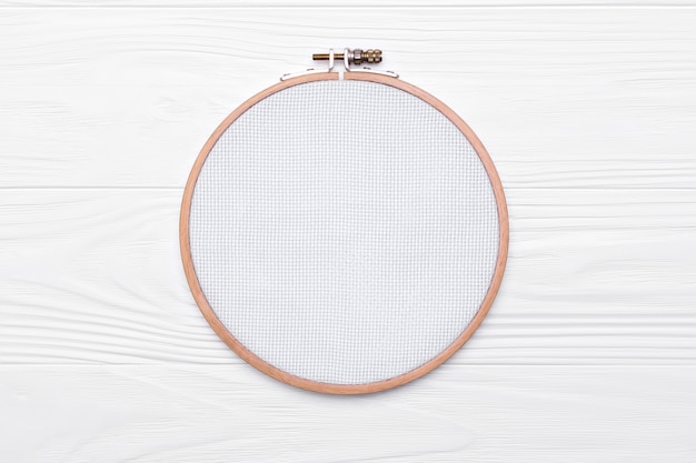 Tools for cross stitch. A hoop for embroidery and canvas on white wooden background.