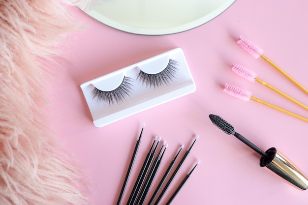 Photo tools for eyelash extension on trendy pastel pink background false eyelashes tweezers and brushes beauty shop makeup cosmetics top view flat lay