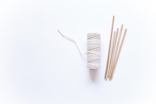 白い表面にマクラメ織りのツールと素材。綿のロープとスティック。