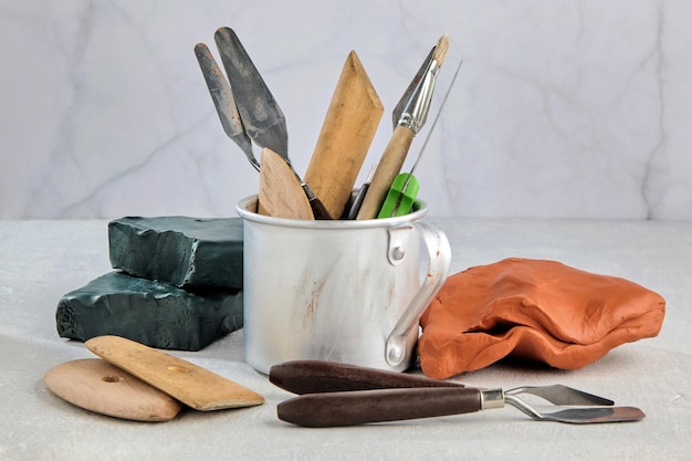 Tools for modeling from plasticine and clay in a metal mug and pieces of clay and plasticine on a white concrete table in a sculpture workshop