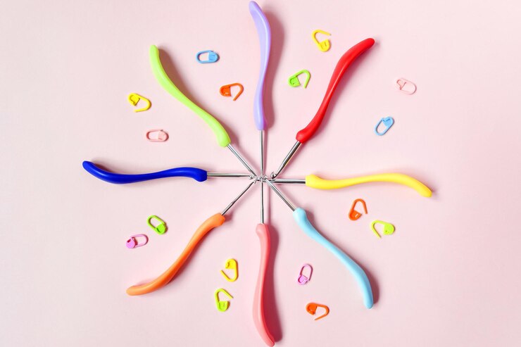Photo tools for needlework hooks of different sizes in form of circle and pins on pink background