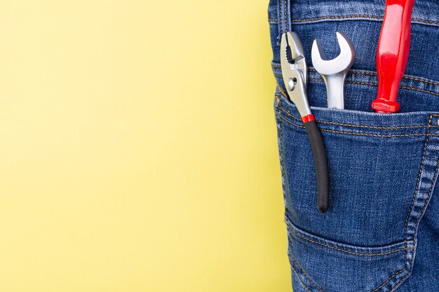 Tools in the pocket of a craftsman jeans on a yellow wall with place for text