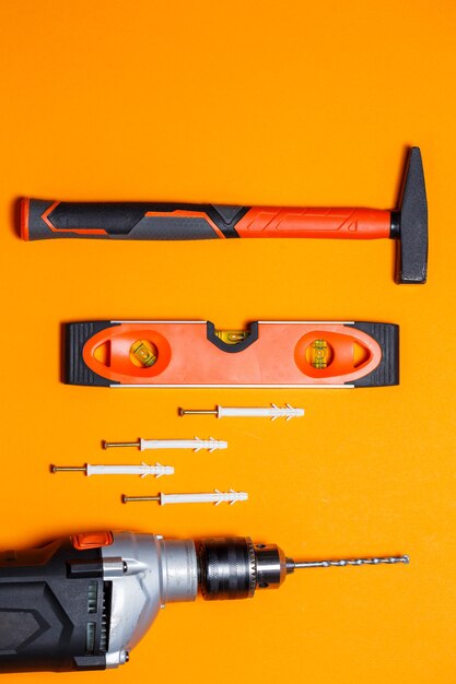 Tools for repairing home use. Hammer for nails, level and drill, dowel in the wall on an orange background. Toolkit for the wizard