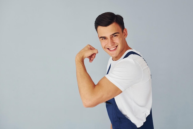 Toont biceps Klaar om te werken Mannelijke werknemer in blauw uniform staande binnenkant van studio tegen witte achtergrond