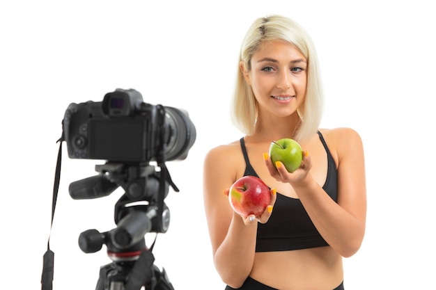 Toont het Kaukasische meisje van de sport rode en groene appelen voor camera, geïsoleerd portret