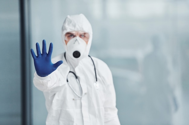 Toont stopgebaar met de hand. Mannelijke arts wetenschapper in laboratoriumjas, defensieve brillen en masker