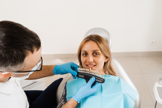歯のカラーシェードを扱う歯のホワイトニング歯科医は、歯科医院で歯のカラーマッチングサンプルをチェックする歯科医をガイドします