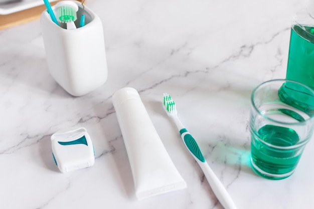 Toothbrush toothpaste mouthwash and dental floss on white marble background Dental hygiene concept