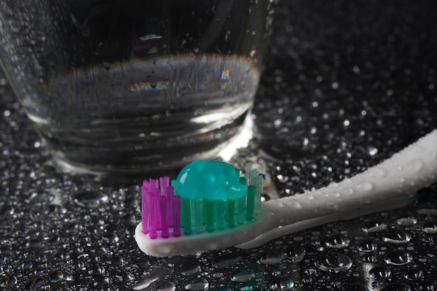 Toothbrush with toothpaste on black background with water drops