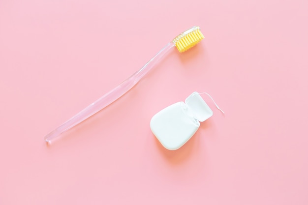 Зубная щетка с желтой щетиной и зубной нитью на розовой стене.