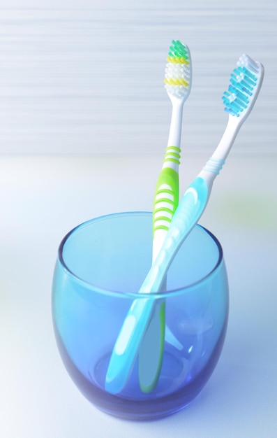 Toothbrushes in glass on table on light background