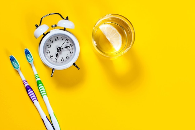 Toothbrushes, glass of water with lemon and alarm clock