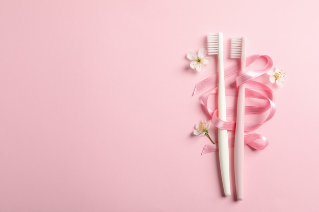 Toothbrushes, ribbon and flowers on pink surface