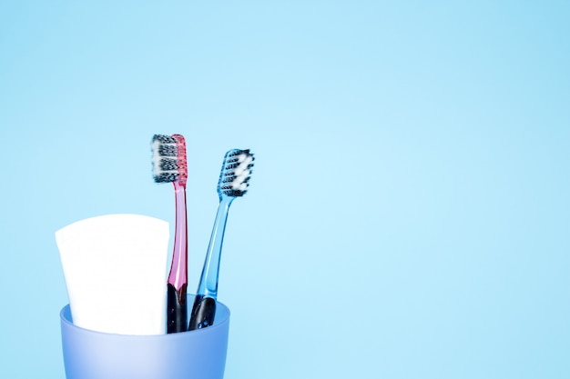 Photo toothbrushes with toothpaste in a glass, blue background. copy space