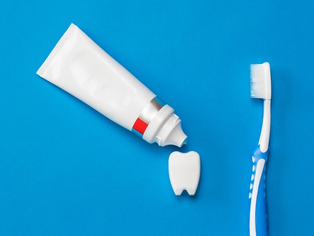 Toothpaste flows out onto a tooth figure and a toothbrush on a blue background Means to care for the oral cavity Flat lay