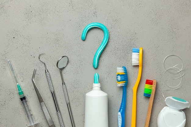 Toothpaste in the form of question mark and many different and colored toothbrushes and dental floss