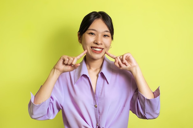 A trentadue denti femmina asiatica che punta le dita al suo sorriso su sfondo giallo