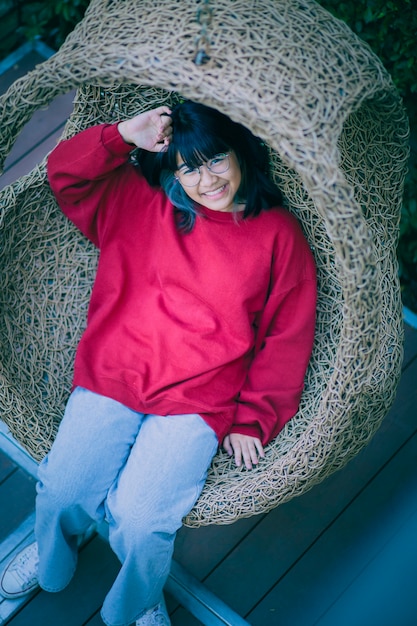 Toothy lachend gezicht van Aziatische tiener zittend in bamboe schommel thuis terras
