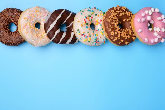 Top boven overhead close-up plat lag flatlay bekijk foto van lekkere stijl veel donuts liggend in een rij geïsoleerd over blauwe pop pastel achtergrond