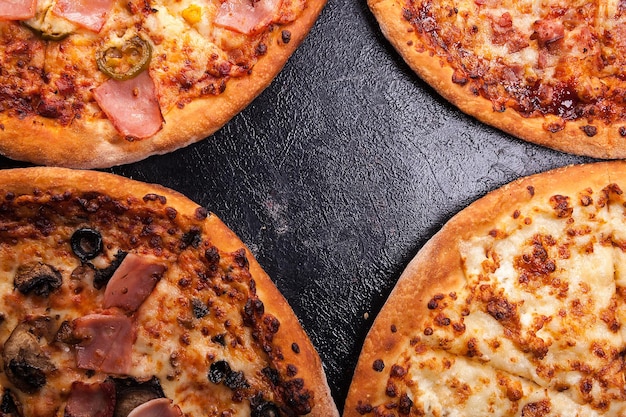 Top close up view of four different pizzas on dark wooden background