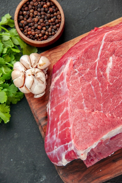 top close view raw meat slice with greens and seasonings on dark surface