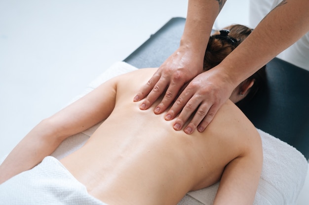 Top closeup view of male masseur massaging back and shoulders of female lying on massage table