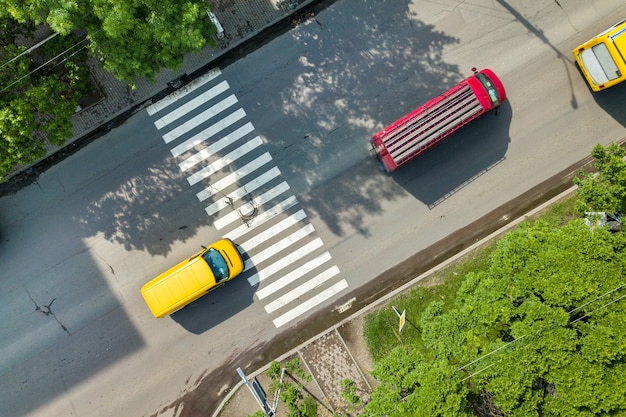 Top down aerial view of busy street with moving cars traffic and zebra road pedestrian crosswalk.