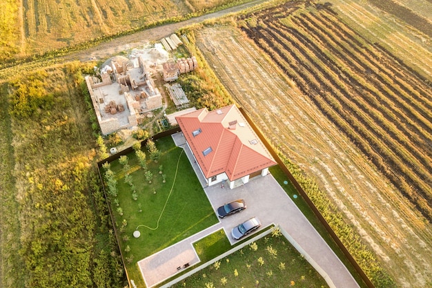 Top down aerial view of two private houses, one under construction with concrete foundament and brick walls and another finished with red tiled roof.