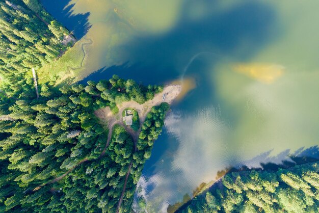 Top-down luchtfoto van groot meer met helder blauw water tussen hoge bergheuvels bedekt met dicht groenblijvend bos.