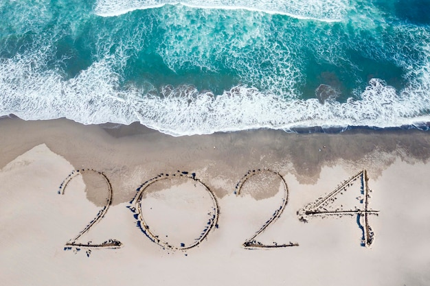 Top down view of 2024 new year numbers written on the sand of coastline