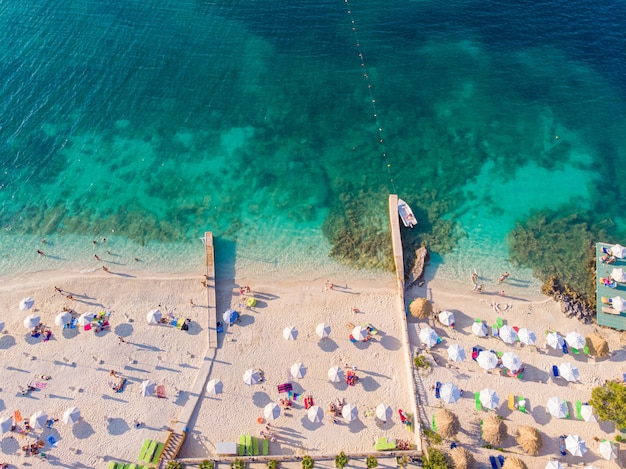 Vista dall'alto verso il basso di una bellissima spiaggia di sabbia bianca con acqua turchese e persone rilassanti in una giornata di sole. ksamil, albania.