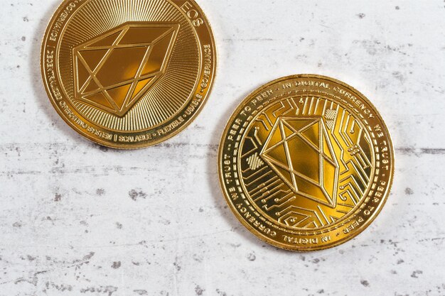 Top down view, detail of golden commemorative EOS - EOSIO cryptocurrency - coins on white stone board.