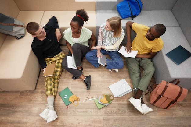 Top down view at diverse group of young students studying together while sitting on floor in college...