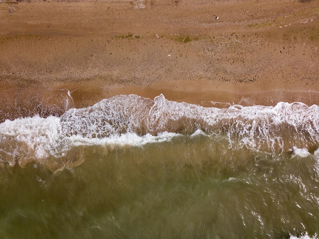 Top down view of waves breaking in the sand, flying over tropical sandy beach and waves