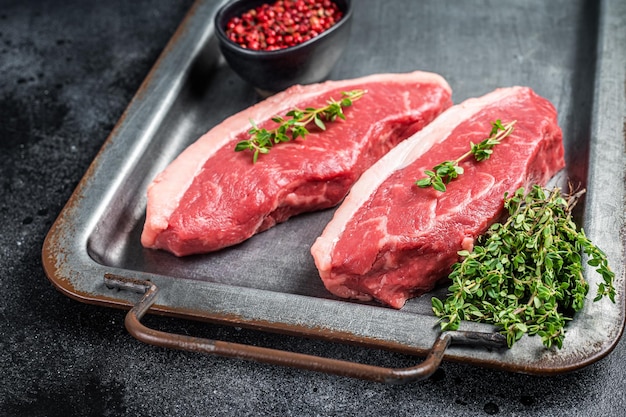 Top entrecote rauwe biefstuk met tijm en peper op stalen dienblad zwarte achtergrond bovenaanzicht