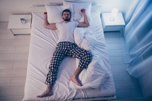 Top above high angle view of his he nice attractive sleepy drowsy guy lying on bed fallen asleep good life lifestyle at night late evening home illuminated room flat house