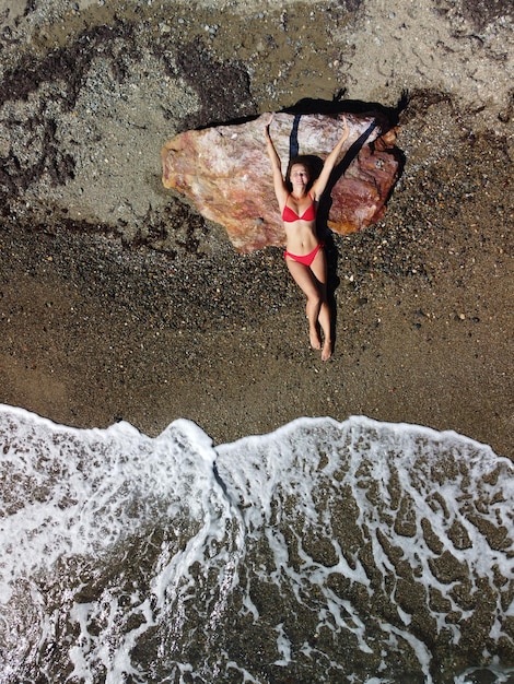 Top luchtfoto op een jonge sensuele blonde vrouw in rode bikini liggend op de rots in de buurt van water op zee