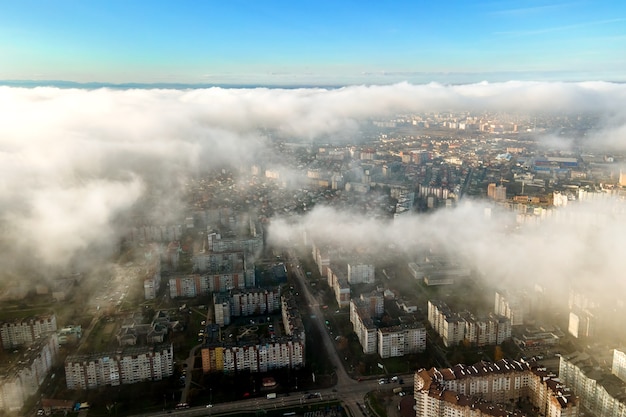 Top luchtfoto van pluizige witte wolken boven moderne stad met hoge gebouwen.