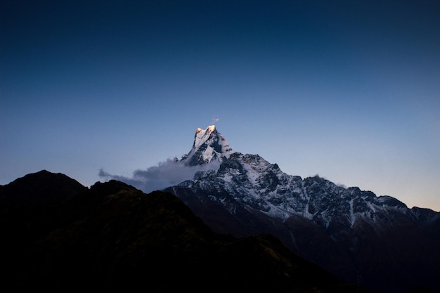 The top of the mountain is lit up with the sun setting behind it.