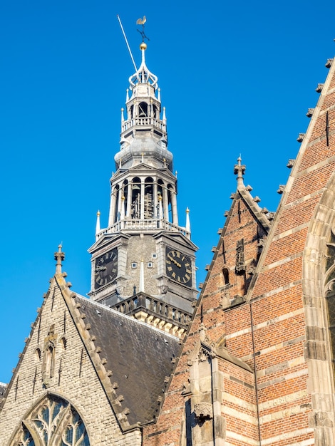 Верхняя часть старой церкви (Oude Kerk) в главном районе красных фонарей в Амстердаме, Нидерланды, под голубым небом