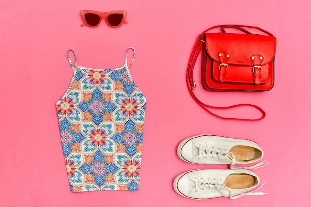 Top in ornament, red handbag, white sneakers and rose colored glasses Bright pink background, close up