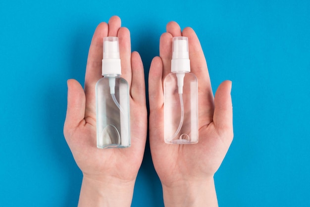 Top above overhead close up first person view photo of female hands holding showing two bottle with antibacterial liquid isolated over blue bright color background