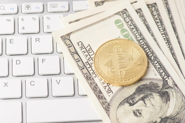 Top above overhead close up view photo image of pile of dollars with laying golden bitcoin with white keyboard buttons on the background