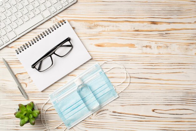 Photo top above overhead flatlay view photo of laptop notebook with eyewear and two medical masks with antiseptic on white wooden backdrop